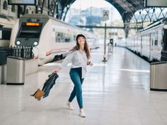 Woman in white long sleeve shirt and blue denim jeans standing on the platform of a train station